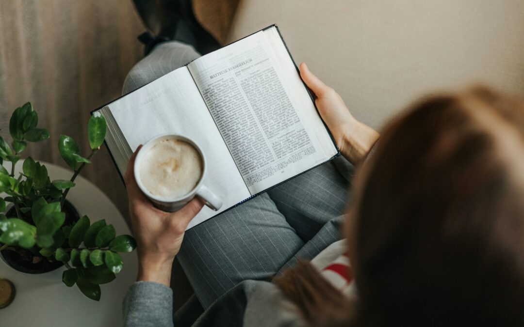a woman reading a book while holding a cup of coffee